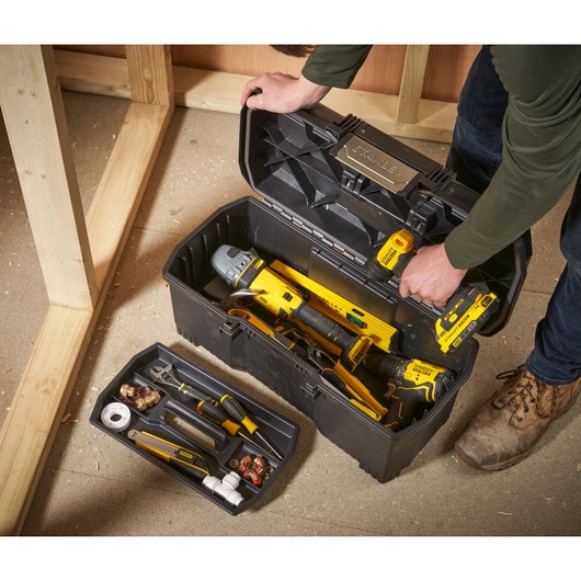STANLEY 1-97-510 toolbox with open lid showing assorted hand tools, drill, and accessories on workshop floor, top angle.