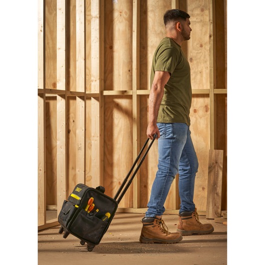 STANLEY 1-97-515 rolling tool bag with tools, carried by person in work boots at construction site.