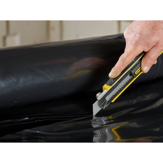 STANLEY 2-11-725 utility knife cutting black plastic sheet, close-up view.