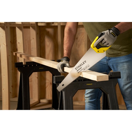 STANLEY 2-15-283 hand saw cutting wood on black sawhorse in workshop, close-up angle.