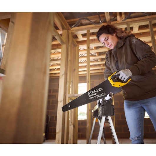 Photo of STANLEY 2-20-180 hand saw with yellow and black handle in use cutting plastic pipe on worksite.