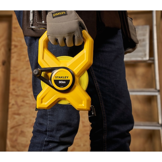 Photo of STANLEY 2-34-792 yellow 30m open reel tape measure held by a worker in gloves, construction setting.