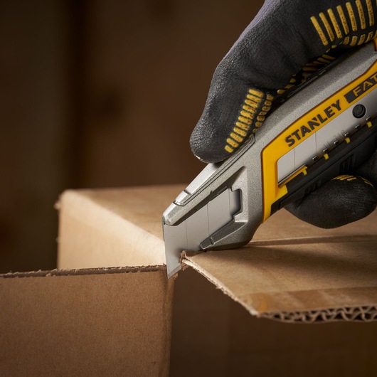 STANLEY 3-11-718 utility knife cutting cardboard, close-up view with gloved hand holding the knife.