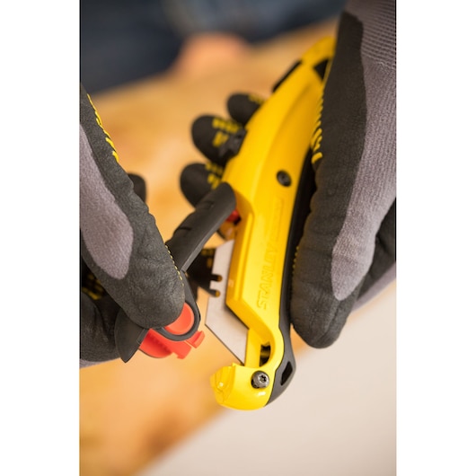STANLEY 7-10-778 yellow utility knife held by gloved hands, close-up showing blade area.