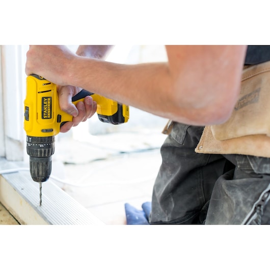 Photo of STANLEY FMC021S2 cordless drill in use, yellow body, drilling into metal surface, close-up view.