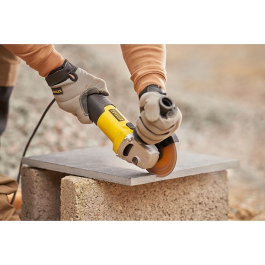 Photo of STANLEY FMEG225VS angle grinder cutting stone slab outdoors, operator wearing work gloves.