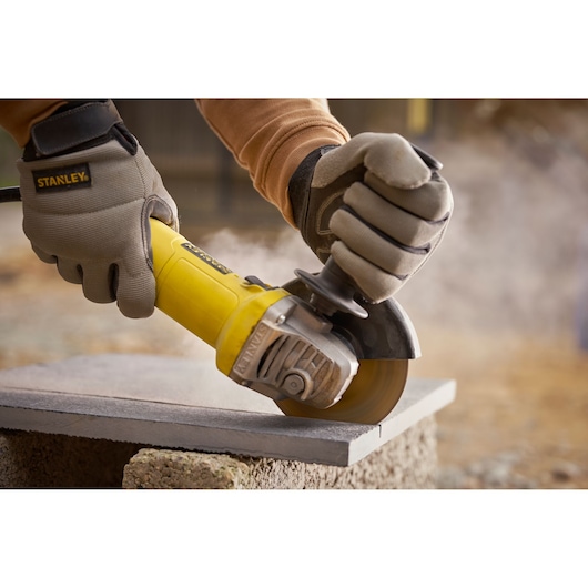 STANLEY FMEG615 angle grinder in use, cutting stone, close-up with work gloves.