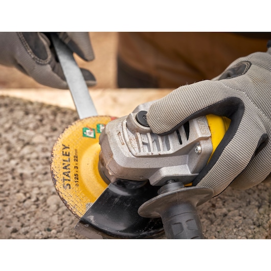 STANLEY FMEG615 angle grinder in use on stone surface, close-up of gloved hands holding tool.