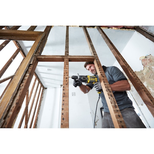 Photo of STANLEY FMEH1100K hammer drill in use on wooden framing, construction setting, side angle.