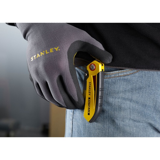 STANLEY FMHT0-10827 folding utility knife in yellow and black clipped to jeans, gloved hand holding it.