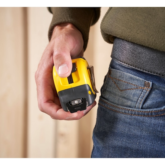 STANLEY FMHT0-33864 tape measure held in hand near jeans pocket, close-up photo.