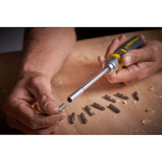 Photo of STANLEY FMHT0-62691 screwdriver set with interchangeable bits on wooden surface, hand inserting a bit.