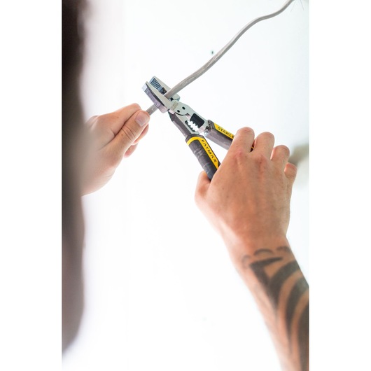 Stanley FMHT0-75469 pliers with black and yellow handles cutting wire, side angle, photography category.