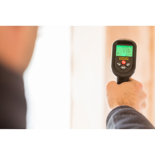 Photo of a hand holding a STANLEY FMHT0-77422 infrared thermometer with illuminated display in use.