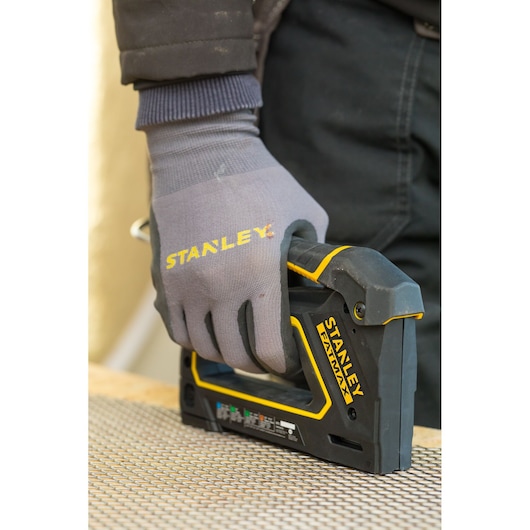 STANLEY FMHT0-80550 stapler in use, held by gloved hand, black and yellow tool on work surface.