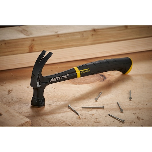 STANLEY FMHT1-51275 claw hammer with black and yellow handle on wooden surface with scattered nails.