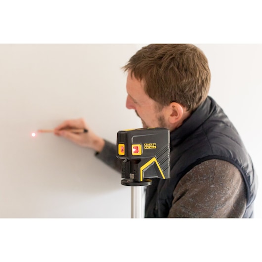 STANLEY FMHT1-77413 laser level on tripod projecting red dot, user marking spot on wall.