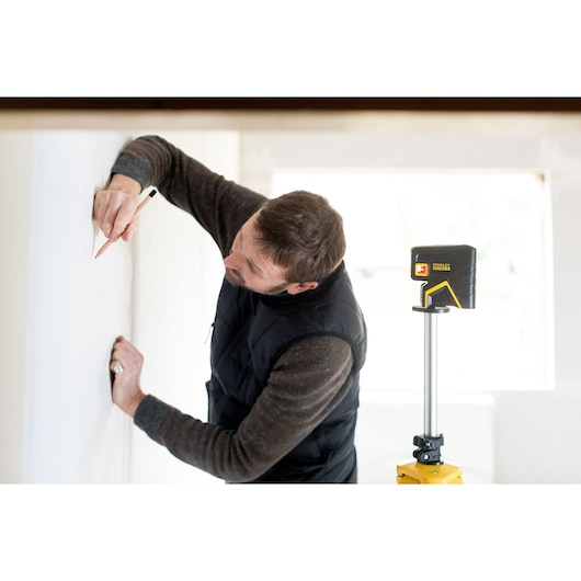 Stanley FMHT1-77413 laser level on tripod beside person marking wall, indoor setting.