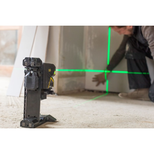 STANLEY FMHT1-77435 laser level projects green lines on wall during construction, side angle view.