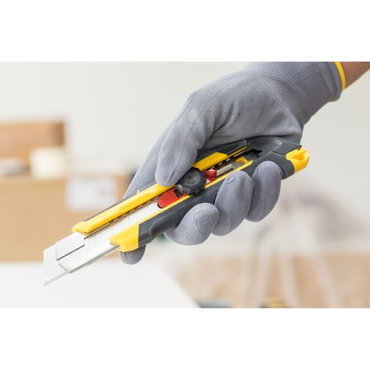 STANLEY FMHT10330-0 utility knife with yellow and black body, held in a gloved hand.