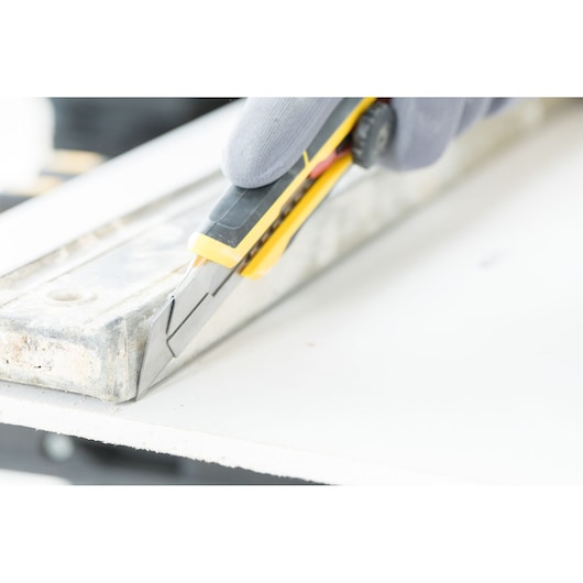 STANLEY FMHT10330-0 utility knife cutting drywall, close-up photo showing blade and yellow handle.