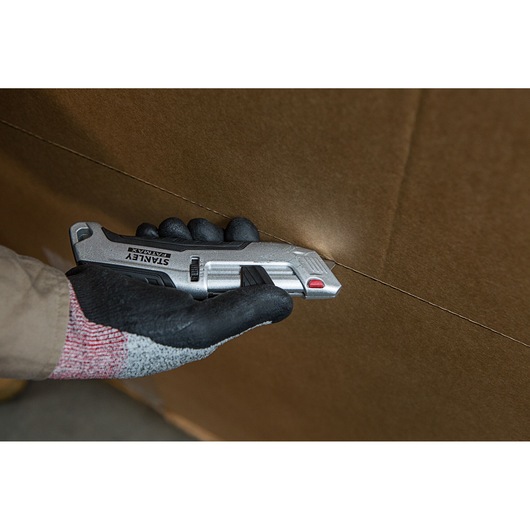 STANLEY FMHT10367-0 utility knife cutting cardboard, close-up of hand holding tool.