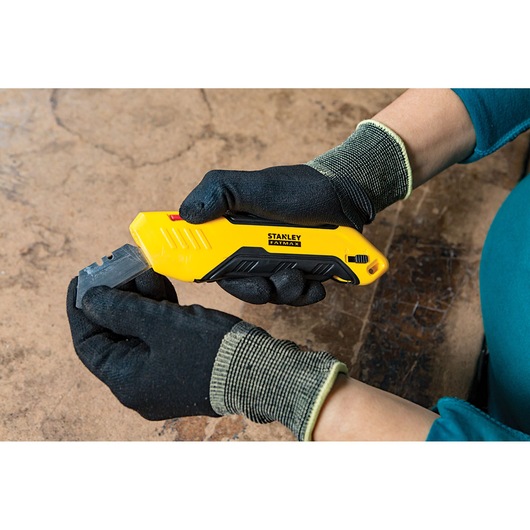 Stanley FMHT10369-0 utility knife with yellow and black handle, held by gloved hands, side view.