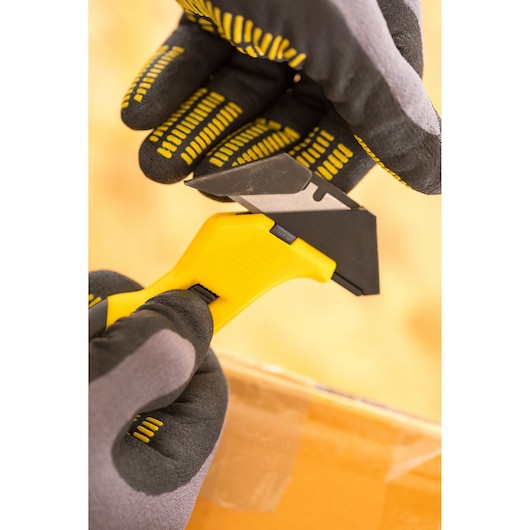 STANLEY FMHT10373-0 safety utility knife with yellow handle, shown in gloved hands cutting tape on a box.