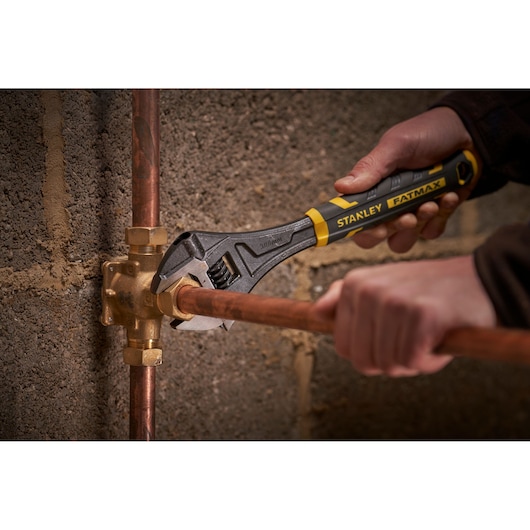 Photo of STANLEY FMHT13126-0 adjustable wrench in use on copper pipe fitting near wall, tool category.