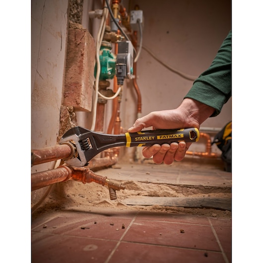 Photo of STANLEY FMHT13127-0 adjustable wrench being used on copper pipes in a plumbing setting.