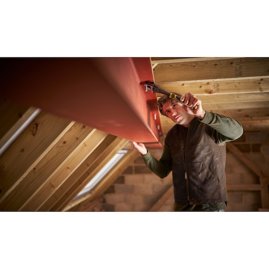 Photo of STANLEY FMHT13128-0 pliers in use tightening a bolt on a red steel beam in a wooden attic.