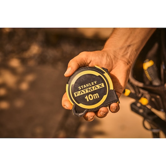 Photo of STANLEY FMHT33005-0 FatMax 10m tape measure held in a hand, black and yellow casing.