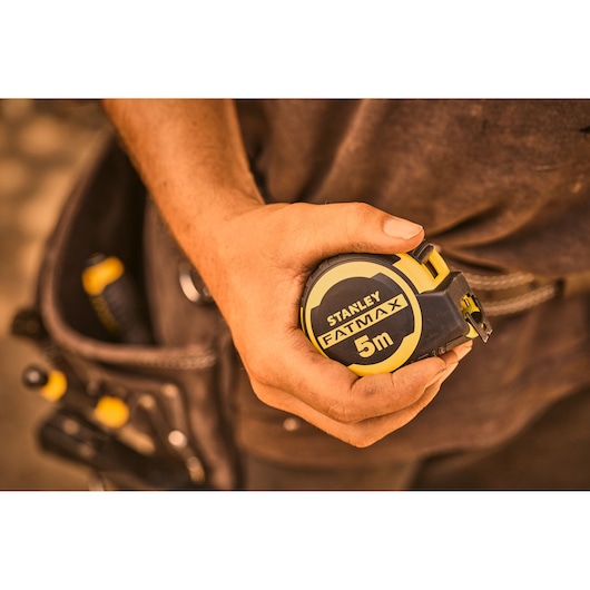 Photo of STANLEY FMHT33100-0 FATMAX 5m tape measure held in hand, tool belt in background.