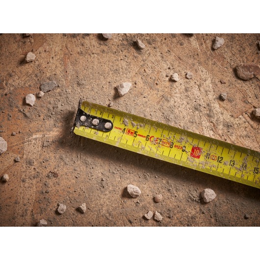 STANLEY FMHT33102 tape measure on dusty concrete with scattered small rocks, close-up view.