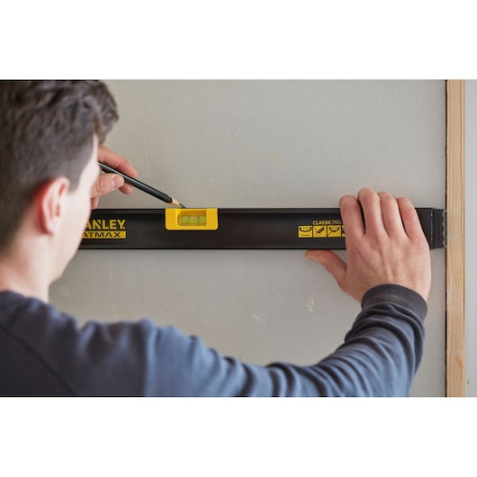 Photo of STANLEY FMHT42554-1 spirit level in use on a wall, person marking line with pencil.
