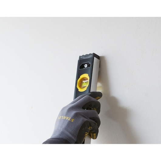 Photo of STANLEY FMHT42561-1 spirit level held vertically against a wall by a gloved hand.