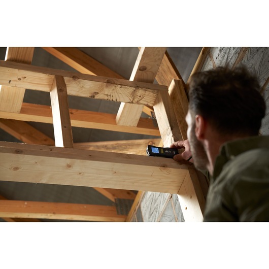STANLEY FMHT77165-0 laser distance measurer used by person to measure wooden beam in construction setting.