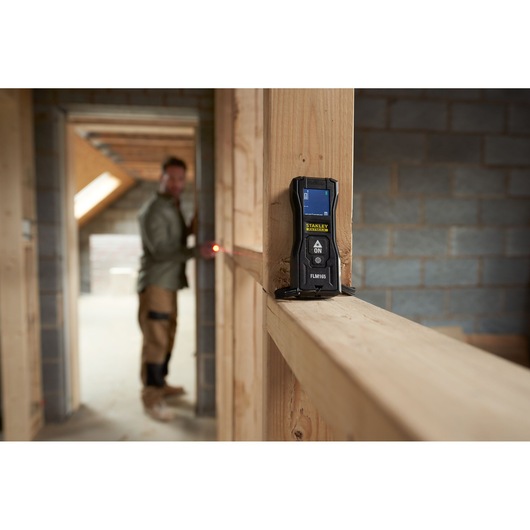 STANLEY FMHT77165-0 laser distance measurer in use on wooden frame, construction setting.