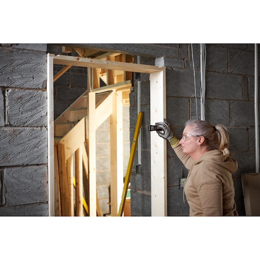 STANLEY FMHT77165-0 laser distance measurer used on wooden door frame at construction site.