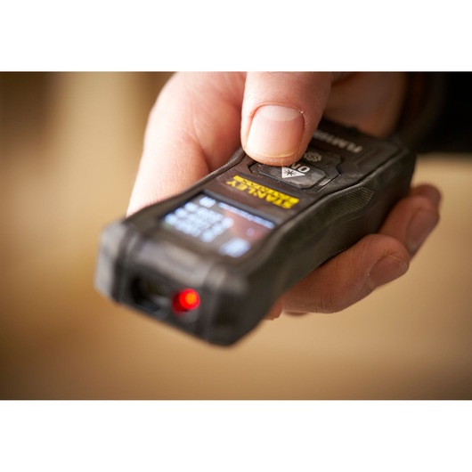 Photo of STANLEY FMHT77165-0 laser distance measurer in hand, front angle showing display and red laser.