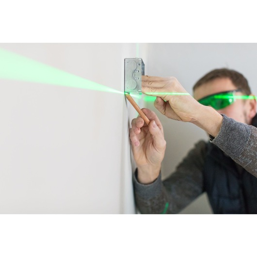 STANLEY FMHT77597-1 laser tool projecting green line for leveling box on wall, photography close-up.