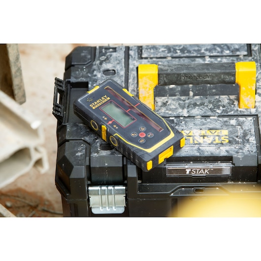 STANLEY FMHT77652-0 laser distance measurer with black and yellow accents on toolbox, angled top view.