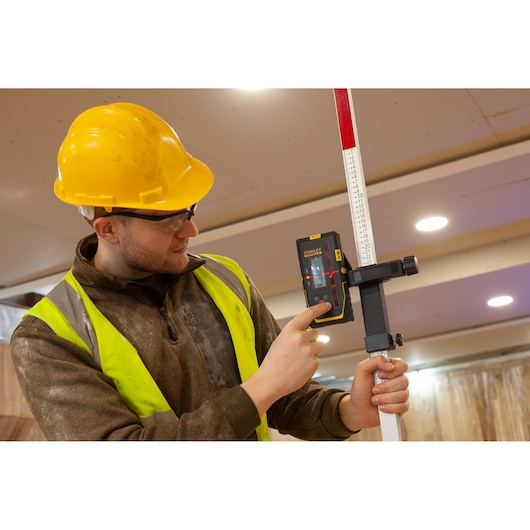 STANLEY FMHT77652-0 laser receiver held by worker on site, attached to measuring rod.