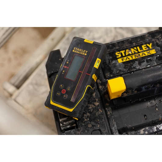 STANLEY FMHT77652-0 laser level device with yellow accents resting on a STANLEY FATMAX toolbox, close-up angle.