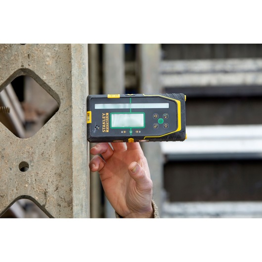 STANLEY FMHT77653-0 laser detector held against concrete by hand, construction site background.