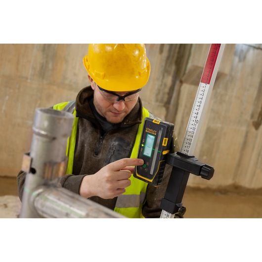 Photo of STANLEY FMHT77653-0 laser receiver mounted on a measuring rod, operated by a worker on construction site.