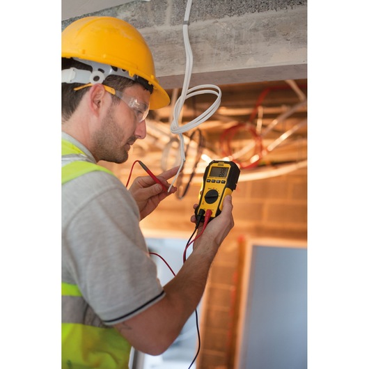 STANLEY FMHT82563-0 digital multimeter used by a worker in a construction setting to test electrical wires.