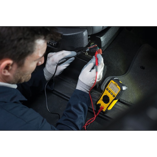 Photo of STANLEY FMHT82563-0 digital multimeter in use testing car wiring, yellow body, clearly visible display.