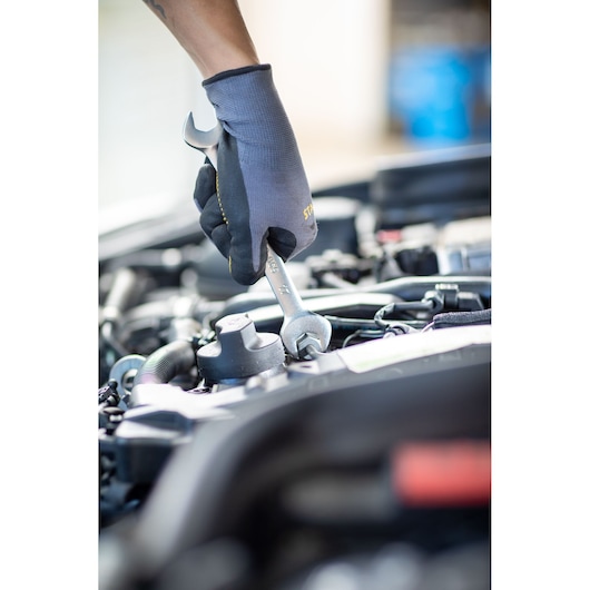 STANLEY FMMT13069-0 wrench in use on car engine, mechanic wearing black gloves, product photography.