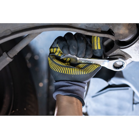 STANLEY FMMT13112-0 wrench in gloved hand tightening bolt, close-up of tool in automotive repair context.